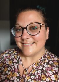 Matante Sylvie Picture of Coach Sylvie, a smiling white woman in her early 40s wearing glasses and a flowery top